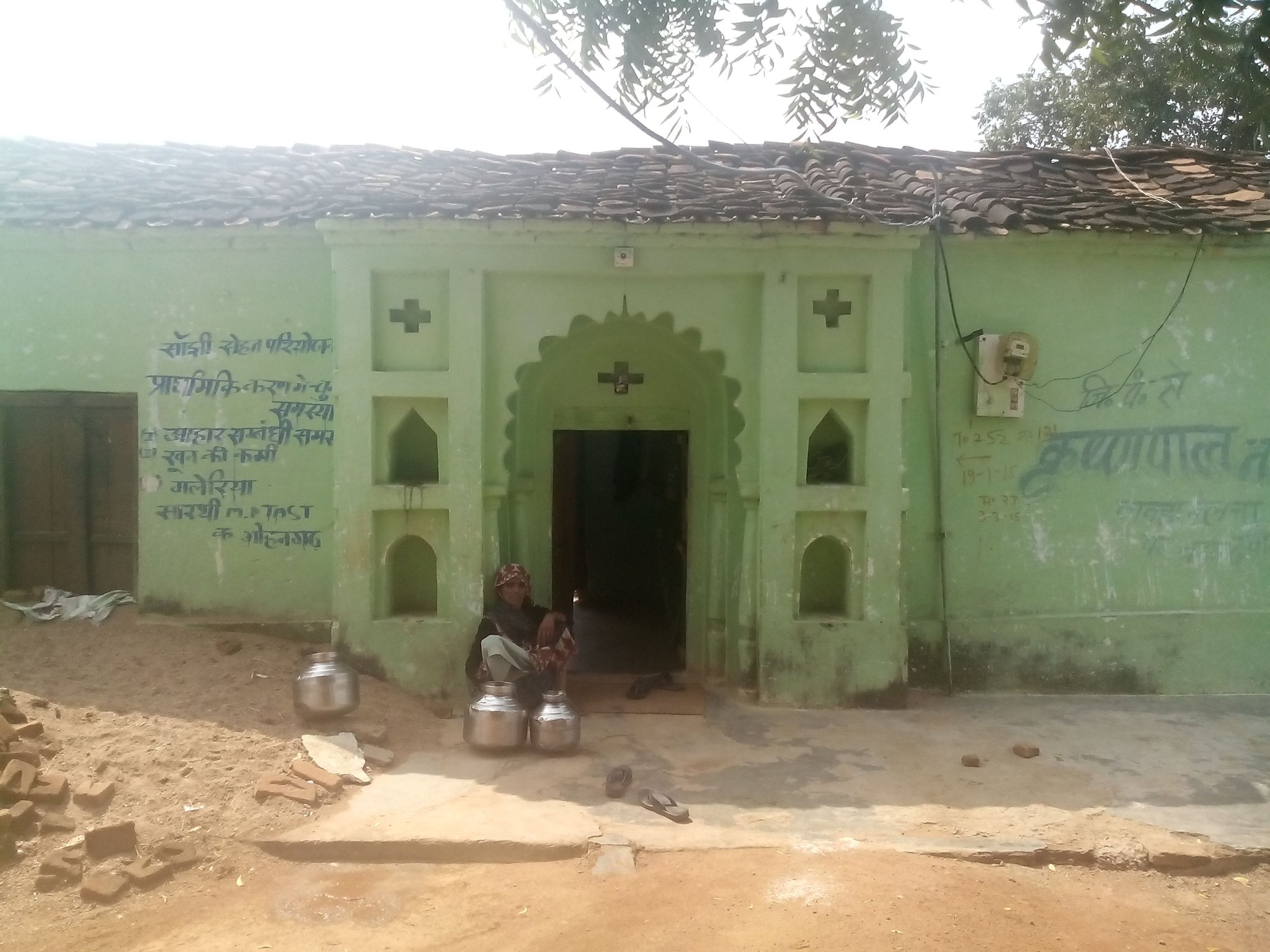 Green-painted village house with steel water pots at the door
